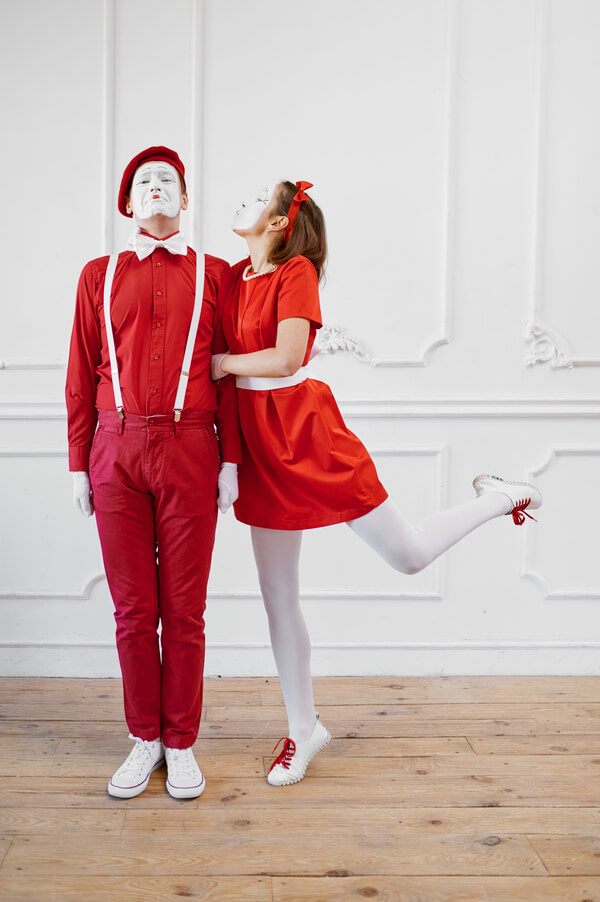 Deux mimes vêtus de rouge et de blanc se tiennent debout sur un plancher en bois. L'homme porte un pantalon, une chemise, un béret, des bretelles blanches et un nœud papillon rouges. La femme, vêtue d'une robe rouge et d'un bandeau, se tient sur une jambe et se penche vers lui comme pour l'embrasser.
