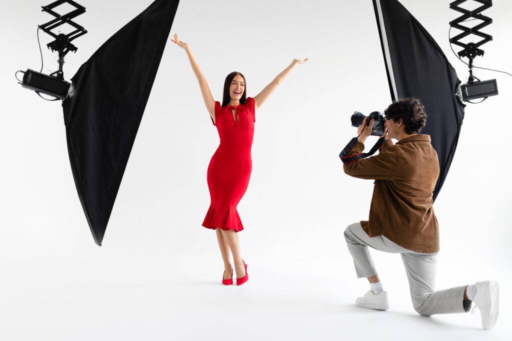 Behind the scenes of photoshoot. Elegant woman posing for professional fashion photographer shooting on white background