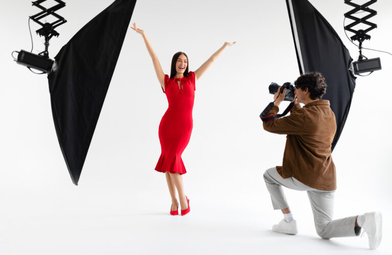 Behind the scenes of photoshoot. Elegant woman posing for professional fashion photographer shooting on white background