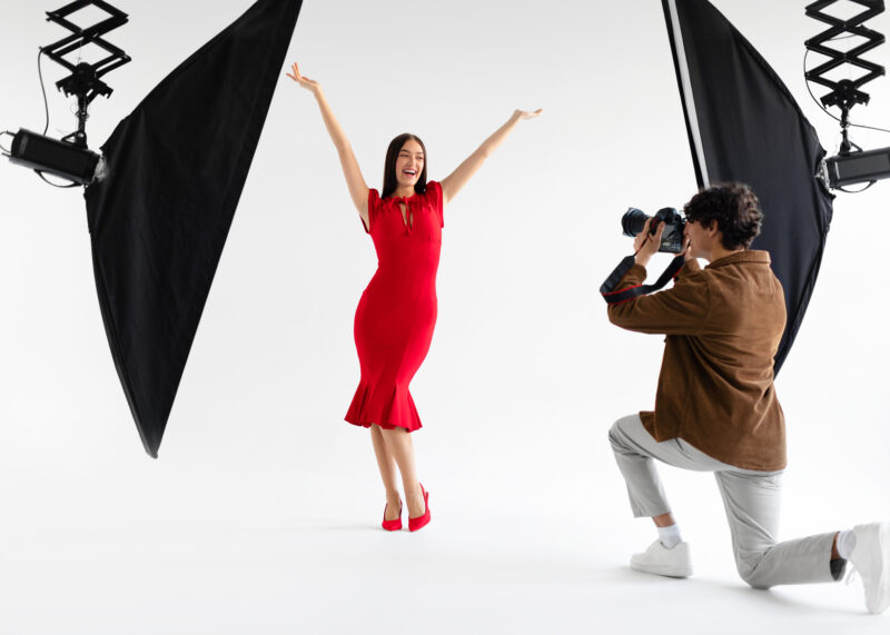 Behind the scenes of photoshoot. Elegant woman posing for professional fashion photographer shooting on white background