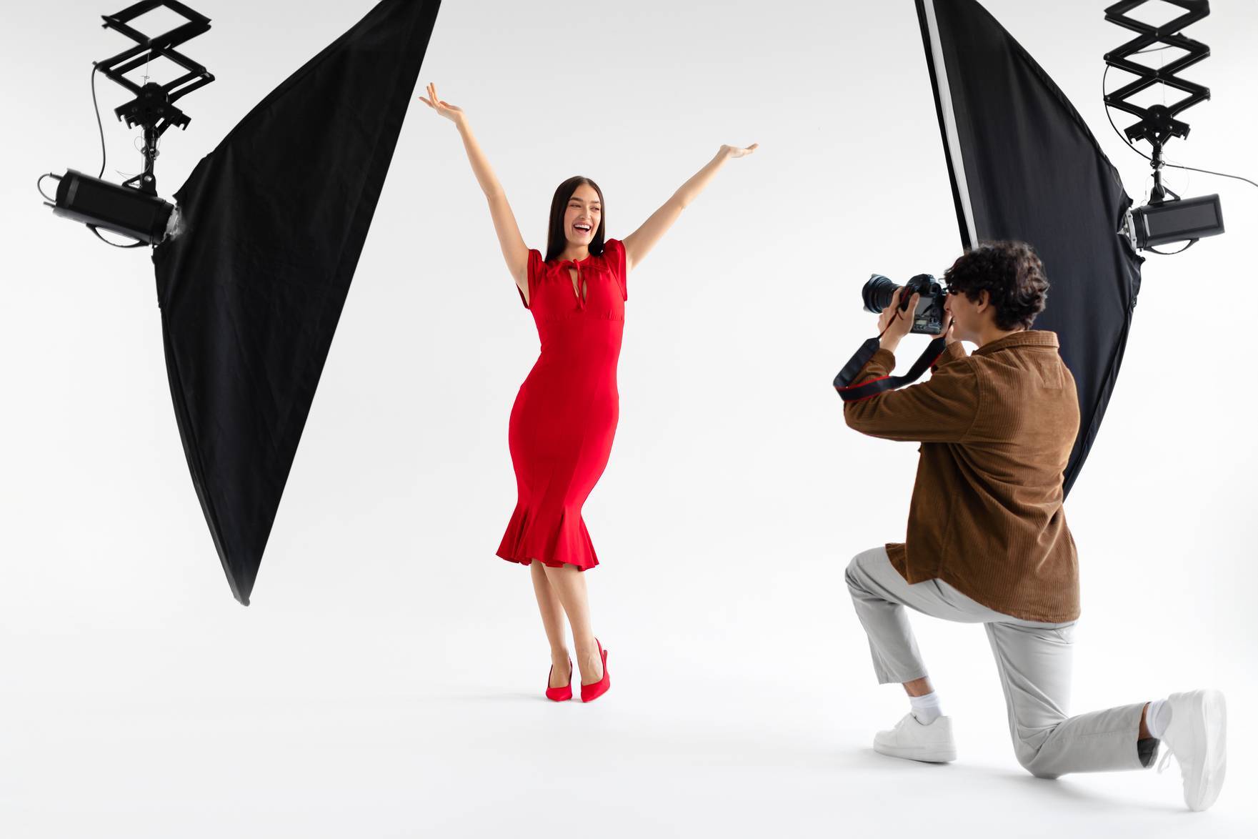Behind the scenes of photoshoot. Elegant woman posing for professional fashion photographer shooting on white background